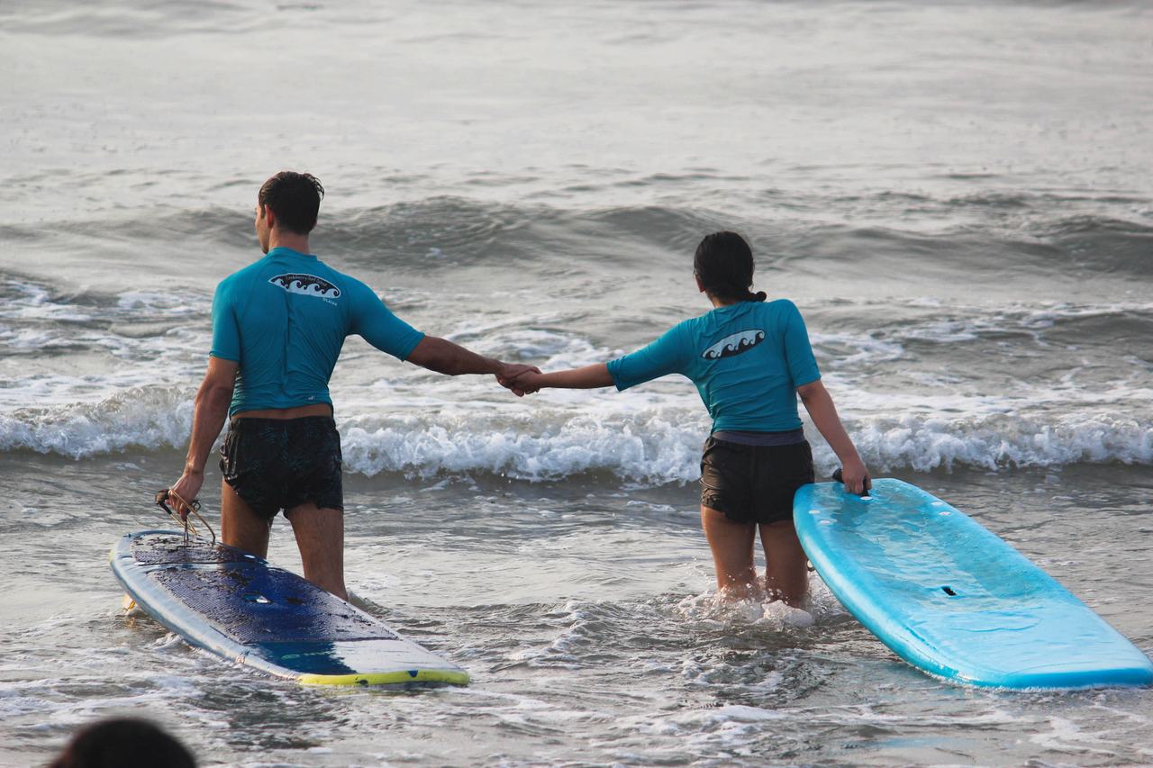 Two students walking into the water with their boards